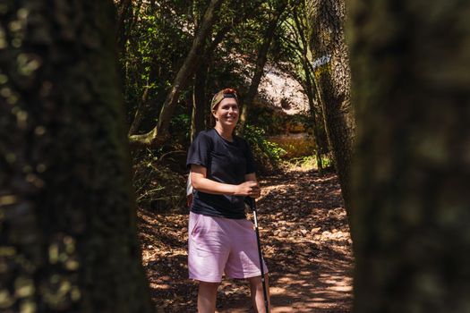 young woman hiking on a forest track. enjoying her holiday. woman walking in nature. hiking poles and mountaineer backpack. natural and warm light. lush vegetation. hiking poles.