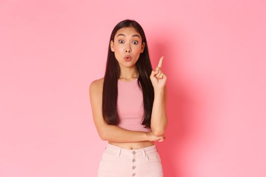 Lifestyle, beauty and women concept. Creative attractive asian girl in summer clothes have solution, raising index finger and saying her idea, think up great plan, standing pink background.