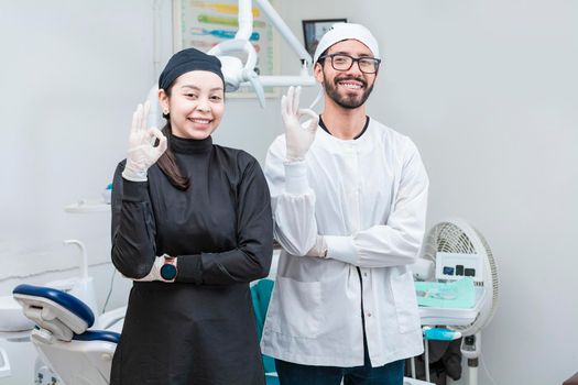 Portrait of dentist and her assistant in the office, female dentist and her assistant thumbs up, oral professionals portrait