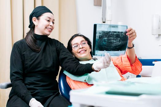 View of dentist with patient reviewing x-ray. Dentist showing x-ray to patient, patient looking at x-ray with dentist, a dentist with x-ray examination