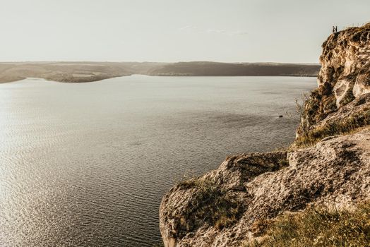 Panoramic view A couple of people in love, a man and a woman, stand on the Big Mountain above the cliff over the sea with islands at sunset. View from a drone on a huge stone rock.