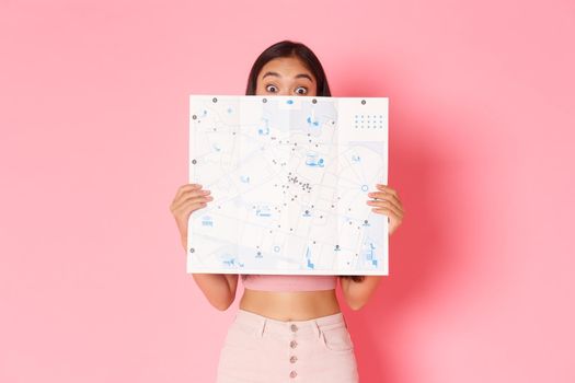 Travelling, lifestyle and tourism concept. Portrait of cute and excited asian girl explore new country, hiding face behind city map and looking amused, tourist going sightseeing or shopping.