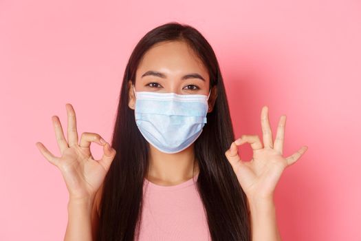 Covid-19 pandemic, coronavirus and social distancing concept. Close-up of excited and amazed pretty asian girl praise great choice, well done or good job gesture, show okay and wear medical mask.