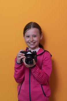 Little girl photographer isolated on yellow background smiling taking photos with a retro vintage camera. High quality photo