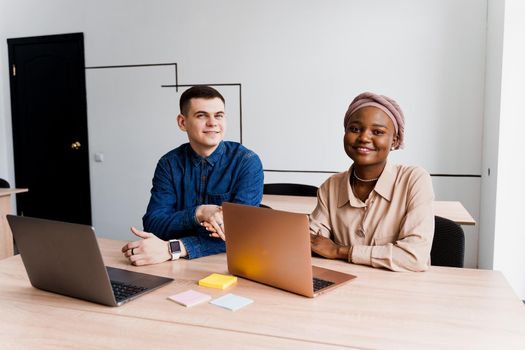 Muslim black girl and white man with laptop. Multiethnic couple work online together on business project. Working at home. Surfing internet.