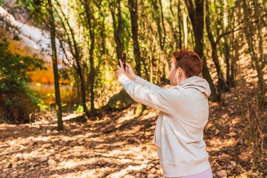 woman lost in the forest, searching for reception signal for her smart phone. accident on vacation. hiking poles and mountaineer backpack. natural and warm light. lush vegetation. hiking poles.