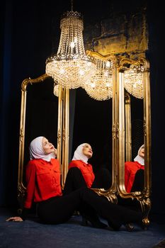 Muslim girl near mirrors with her reflections. Fashion muslim model near big expensive chandelier. Islamic religion