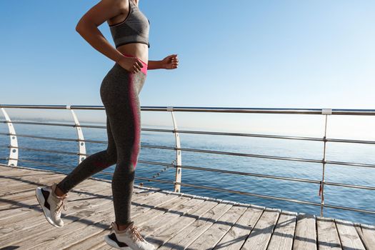 Cropped shot of female running along the seaside, jogging and working out near the sea.