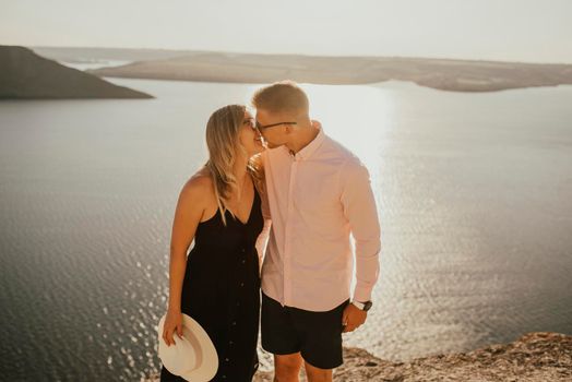 A man and a woman in love walk on a mountain above a large lake by the sea at sunset. A couple of fair-haired fair-skinned people in love are resting in nature in a field