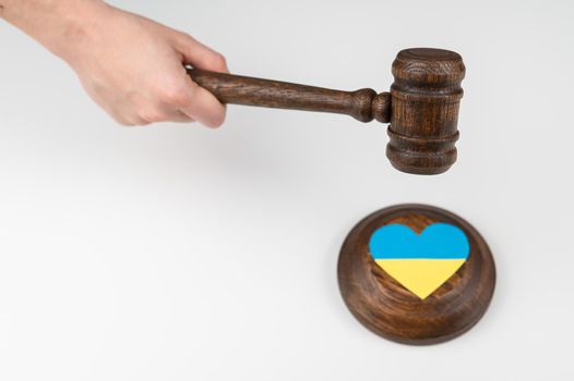 Woman hitting the judge's gavel on the heart with the flag of Ukraine on a white background