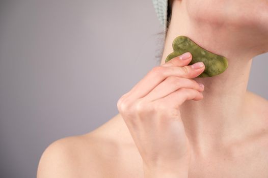 Close-up portrait of a young woman massaging her neck with a gouache scraper