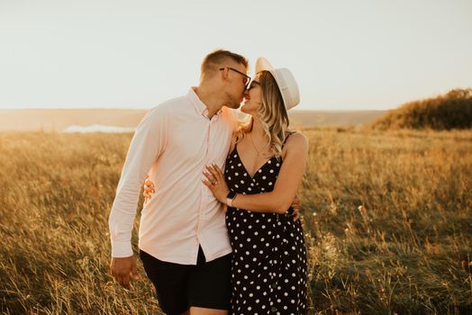 a guy with a girl in hat walking in the meadow. A couple of fair-haired fair-skinned people in love are resting in nature in a field at sunset.