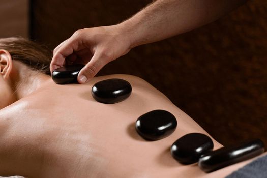 Masseur placed hot stone on the back of woman. Manual therapy in spa