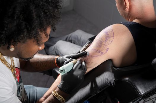 Professional African American tattoo artist makes a tattoo on client arm. High quality photography.