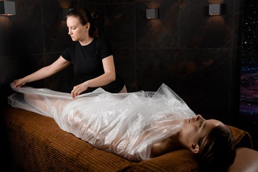 Woman wrapped in a polyethylene wrap. Chocolate Spa therapy.