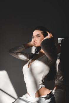 portrait of beautiful gentle woman in a white bodysuit posing in the sunshine. Black long hair. sensuality and tenderness.