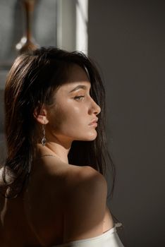 portrait of beautiful gentle woman in a white bodysuit posing in the sunshine. Black long hair. sensuality and tenderness.