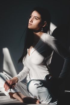 portrait of beautiful gentle woman in a white bodysuit posing in the sunshine. Black long hair. sensuality and tenderness.