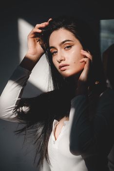 portrait of beautiful gentle woman in a white bodysuit posing in the sunshine. Black long hair. sensuality and tenderness.