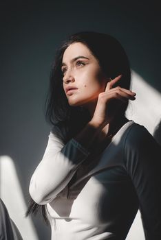 portrait of beautiful gentle woman in a white bodysuit posing in the sunshine. Black long hair. sensuality and tenderness.