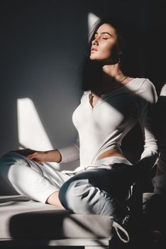 portrait of beautiful gentle woman in a white bodysuit posing in the sunshine. Black long hair. sensuality and tenderness.