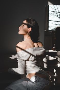 portrait of beautiful gentle woman in a white bodysuit posing in the sunshine. Black long hair. sensuality and tenderness.