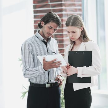 colleagues looking at the screen of the tablet computer while standing in the office.