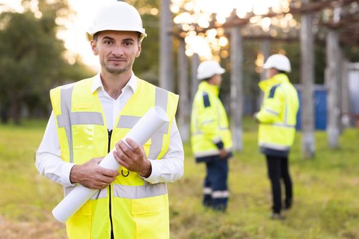 Portrait of engineer. Professional electrical industry engineer smiling and looking at the camera . Workers wearing safety uniform and hard hat with high voltage electrical lines background.