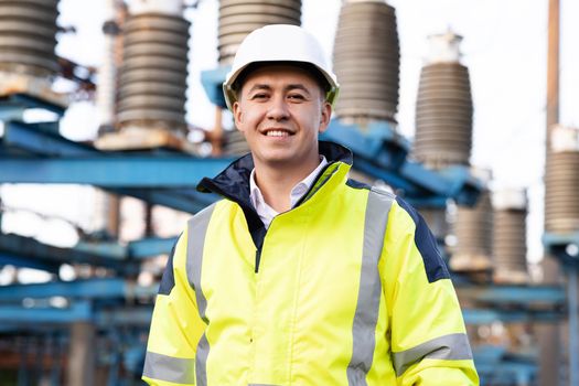 Industrial people. Sustainable energy. Portrait of asian ecology worker in hard hat standing at high voltage power station. Technology.