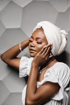 Beauty portrait of black muslim woman weared white dress and headscarf on gray background. Softness and wellness of body and skin,