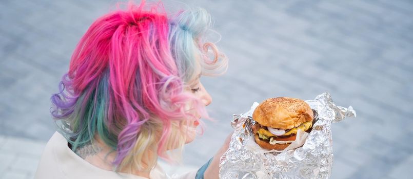 Caucasian woman with curly colored hair eating burger. Bad eating habits and love of fast food.