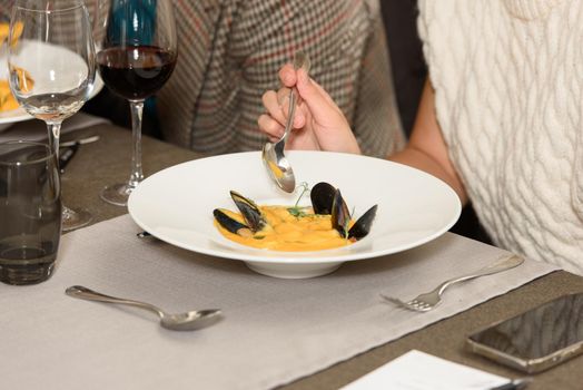 close photo of a woman eating cream soup with seafood in a restaurant