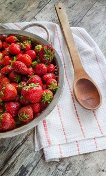 Fresh strawberries in metal sieve. Near wooden spoon and kitchen towel. Overhead view