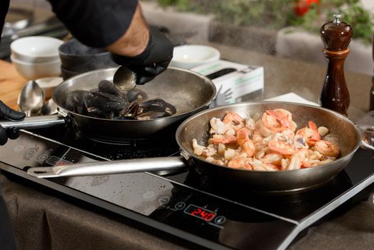 Fried red shrimps with garlic in olive oil in a metal pan on stove. Step by step cooking of sea food pasta.