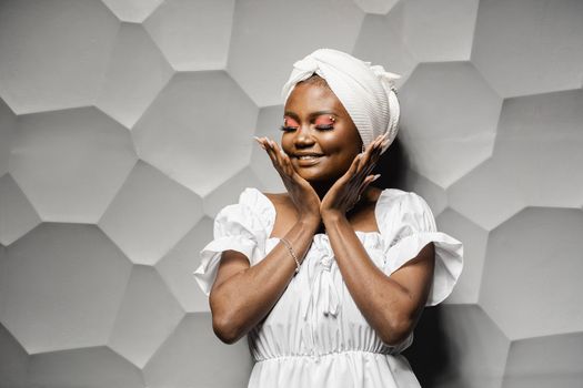 Beauty portrait of black muslim woman weared white dress and headscarf on gray background. Softness and wellness of body and skin,