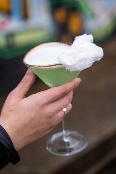 Green alcohol cocktail in glass decorated with cotton candy on color background