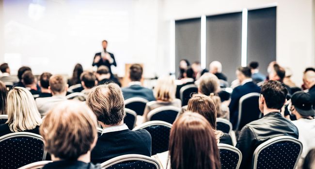 Speaker giving a talk in conference hall at business event. Rear view of unrecognizable people in audience at the conference hall. Business and entrepreneurship concept