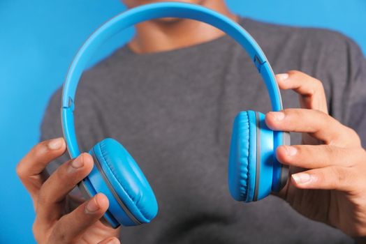 Man hand holding headphone on blue background .