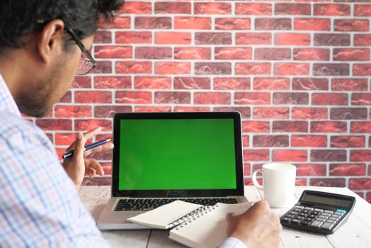 rear view of young man using laptop with blank screen on office desk