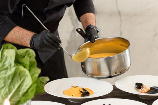 chef prepares set of carrot cream soup with seafood in a restaurant