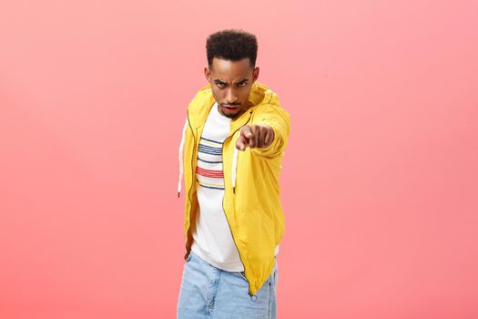 You will regret this. Portrait of threatening angry and pissed dangerous african american young man looking from under forehead with disdain and rage pointing at camera blaming someone over pink wall.