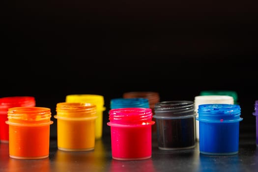 close-up background of opened small gouache paint jars on flat black surface