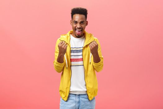 Man being carried away with emotions cheering, being supportive yelling to encourage favorite team play better clenching fists in excitement and making focused expression over pink wall. Copy space