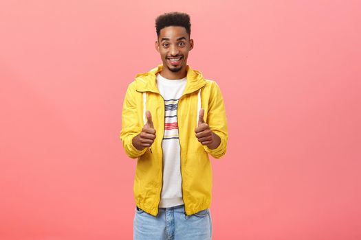 Portrait Lifestyle. Charming friendly boyfriend being supportive and optimistic giving thumbs up and smiling broadly boosting confidence of friend approving his idea posing pleased and delighted over pink wall.