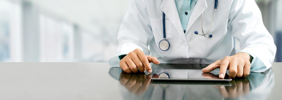 Male doctor sitting at table with tablet computer in hospital office. Medical healthcare staff and doctor service.