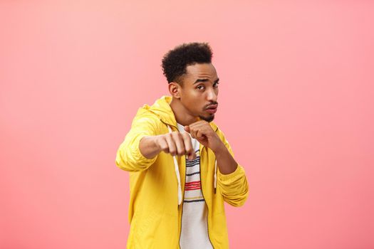 Guy acting cool bragging in front of girlfriend with mascules showing boxer moves standing in boxing pose with raised fist in punch gesture turning right as if fighting over pink background. Emotions concept