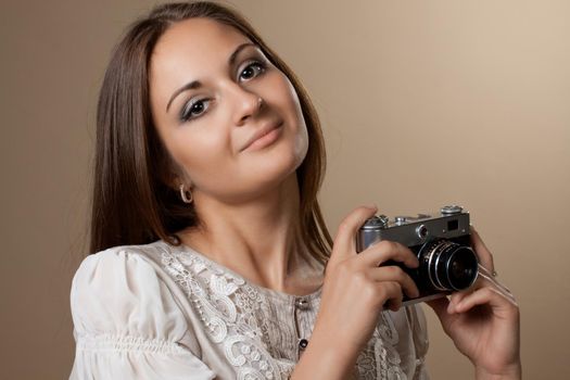 Young brown haired woman in beautiful dress holding retro camera in hands on neutral warm background