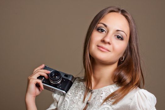 Young brown haired woman in beautiful dress holding retro camera in hands on neutral warm background