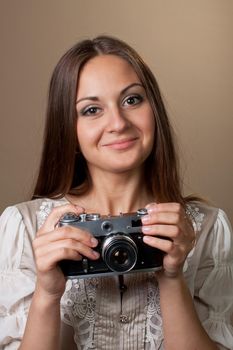 Young brown haired woman in beautiful dress holding retro camera in hands on neutral warm background