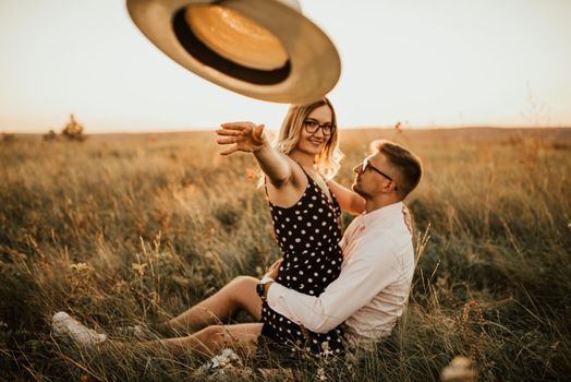 woman throws hat straight at camera. young man and woman in meadow at sunset in summer. A couple of fair-haired fair-skinned people in love are resting in nature